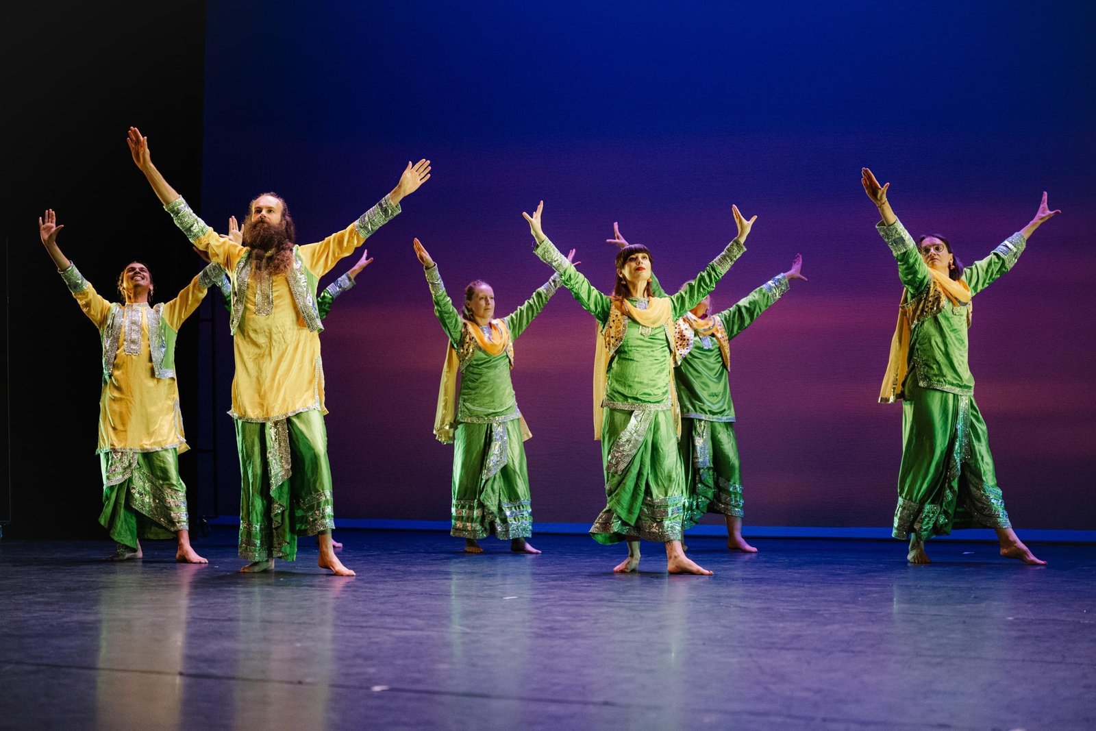 Bhangra students, arms raised in a diagonal line, yellow and green costumes.