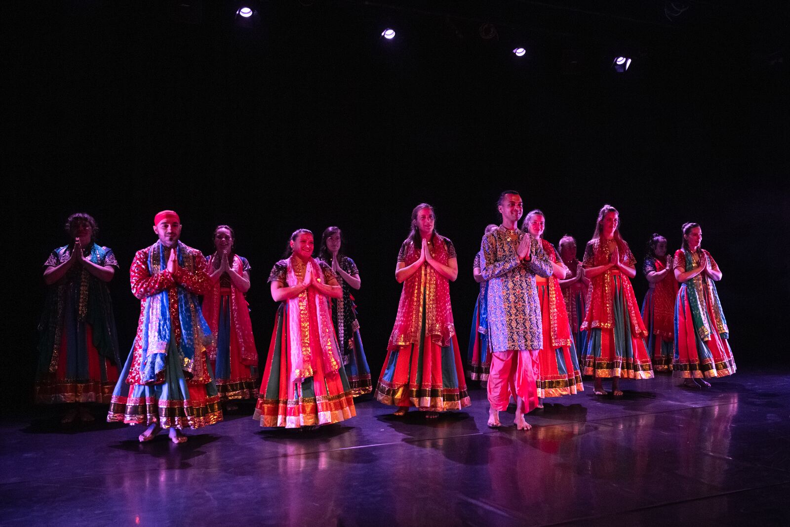 Bollywood students filling the stage in bright red and pink costumes.